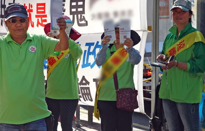 Il gruppo sostenuto dalla CCP L'associazione della gioventù di Hong Kong (HKYCA) ha stabilito delle cabine di informazioni accanto al Falun Gong e usa le proprie bandiere, altoparlanti e volantini per castigare e imitare il Falun Gong. Nella foto, i membri di HKYCA in verde stanno tenendo volantini lanciati a Mong Kok il 16 aprile 2015. (Epoch Times)