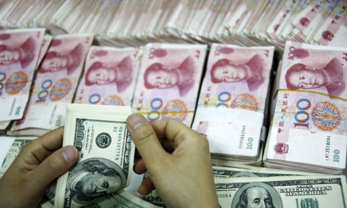 Banconote in dollari americane accanto a pile di cento yuan cinesi. La manipolazione della valuta e il forte affidamento sulle esportazioni da parte della Cina, è una strategia che sta ora rivelando i suoi effetti deleteri. (STR/AFP/Getty Images) 