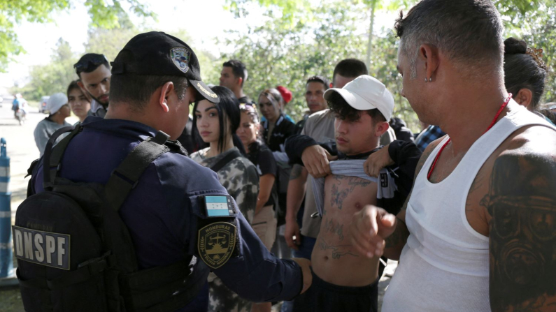 Un agente di polizia controlla il tatuaggio di un migrante per escludere che non sia affiliato a Tren de Aragua, a un posto di blocco a Danli, Honduras, 22 aprile 2025. (Leonel Estrada/Reuters)
